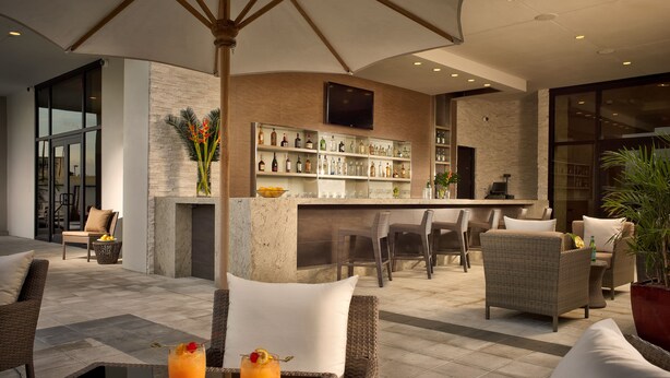A modern outdoor bar area with wicker furniture, a bar counter, and a variety of bottles.