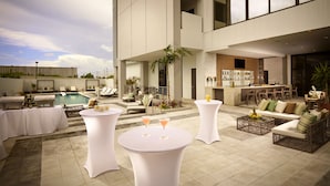 A rooftop bar with a pool, lounge chairs, and a bar area with a view of the city skyline.