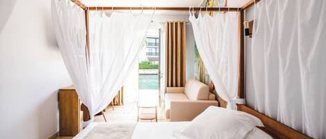 A bedroom with a bed, a wooden headboard, a wooden nightstand, a beige sofa, and a view of the outdoors.