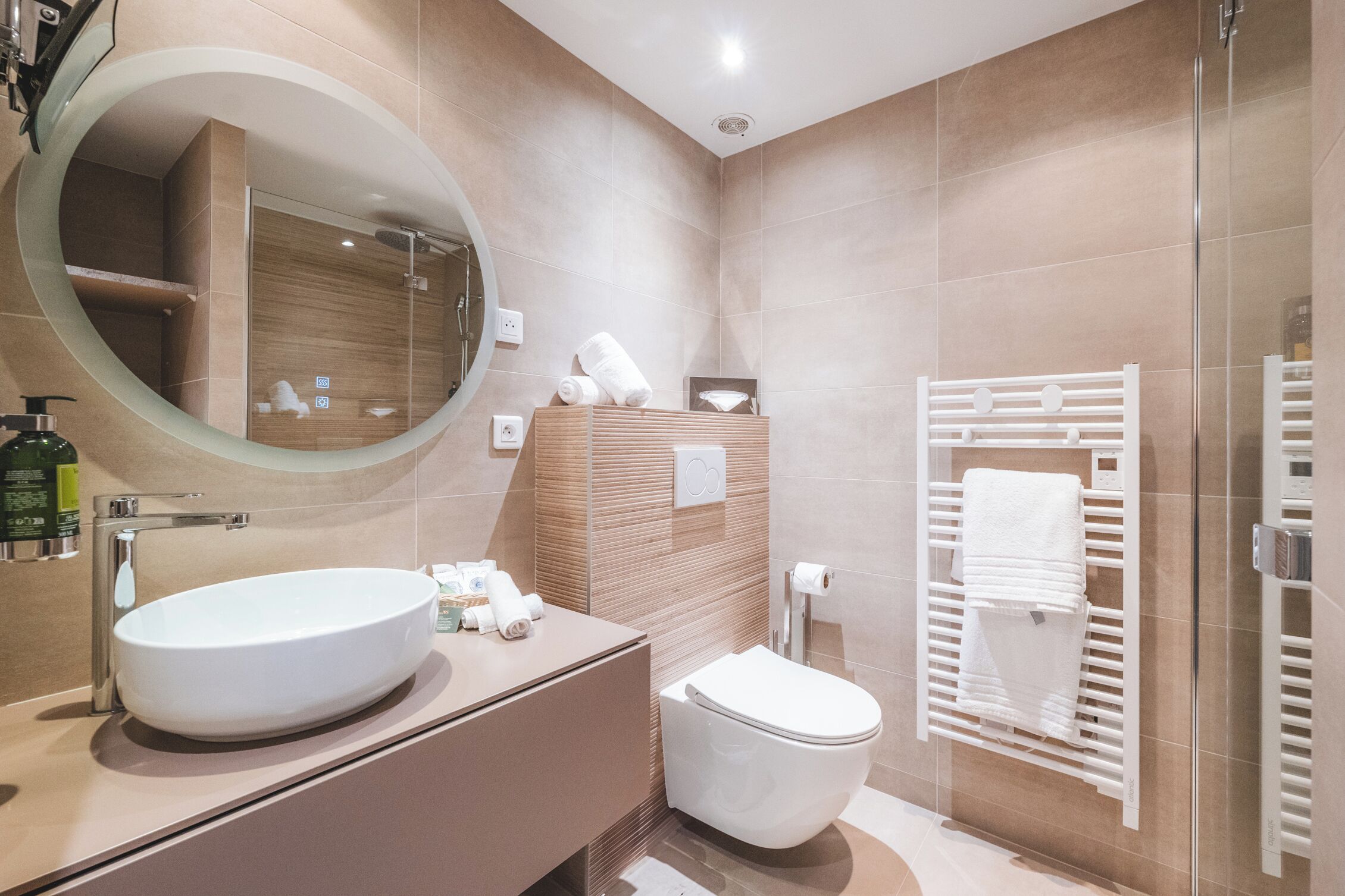 A modern bathroom with a large oval sink, a toilet, a glass-enclosed shower, and a towel rack.