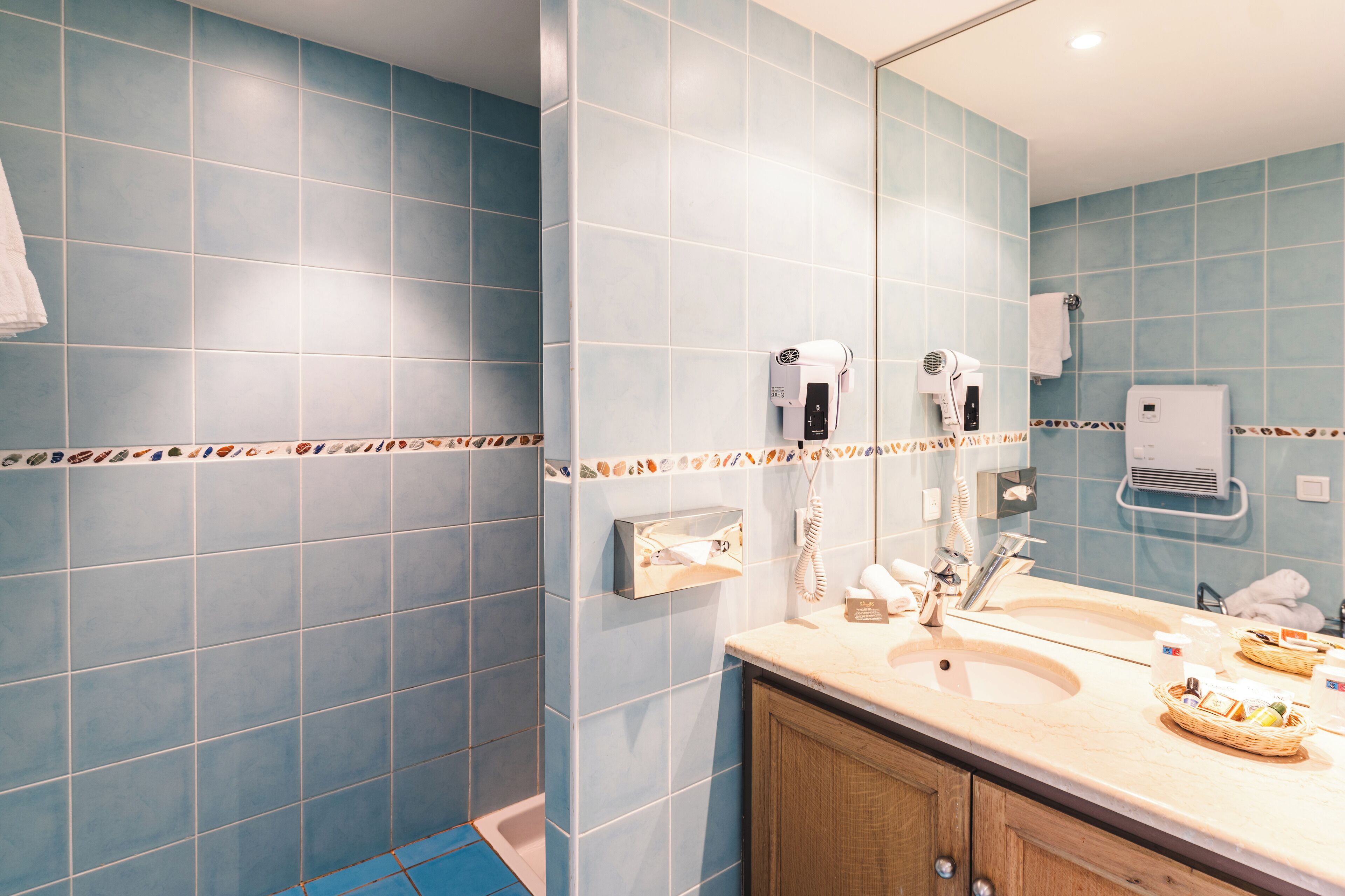 A bathroom with blue tiles, a sink, a mirror, and a hairdryer.