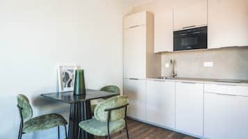 Una cocina compacta con armarios blancos, un horno negro y una pequeña mesa de comedor con cuatro sillas.
