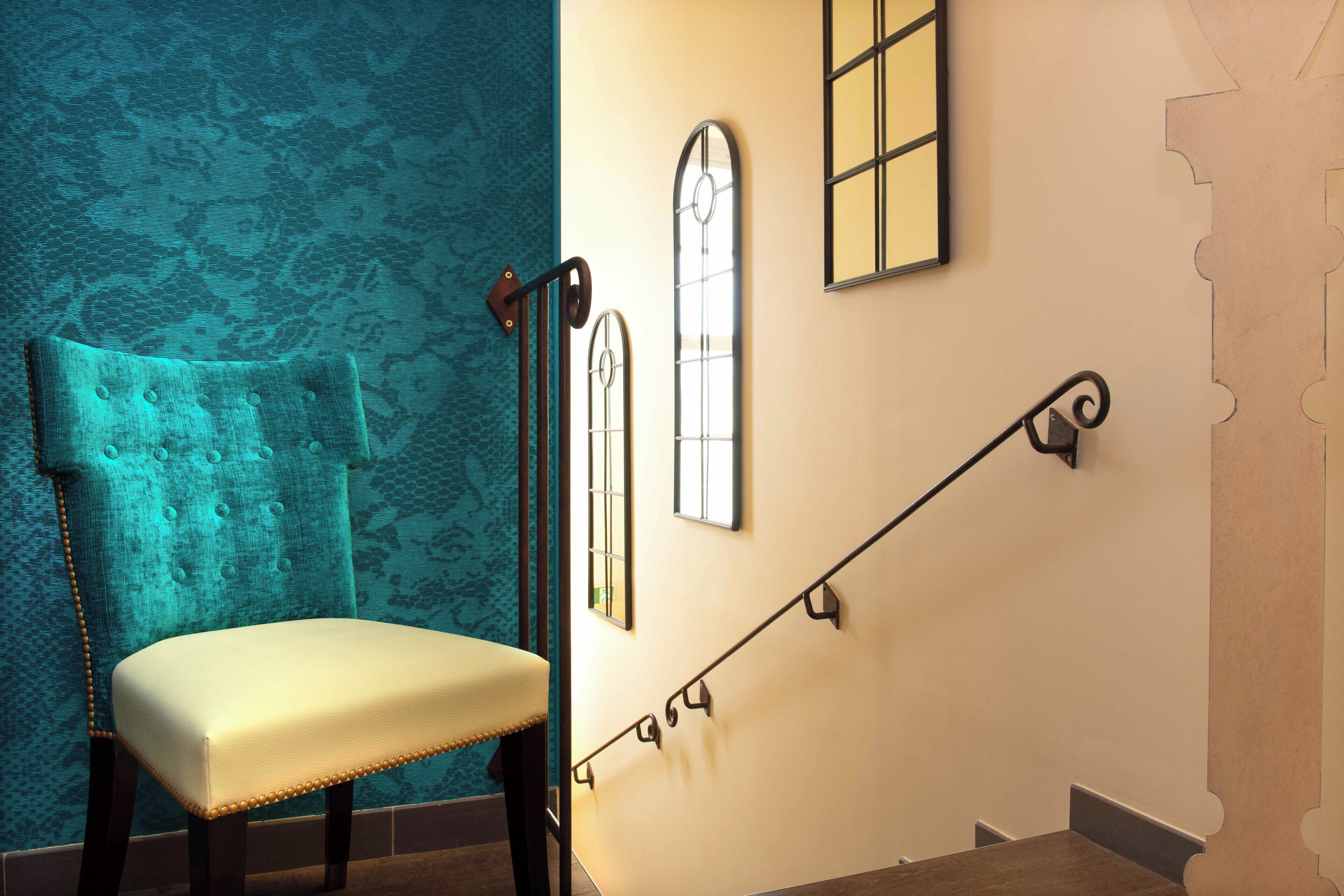 Un escalier avec une rampe métallique, une chaise avec un siège rembourré et un papier peint à motifs.