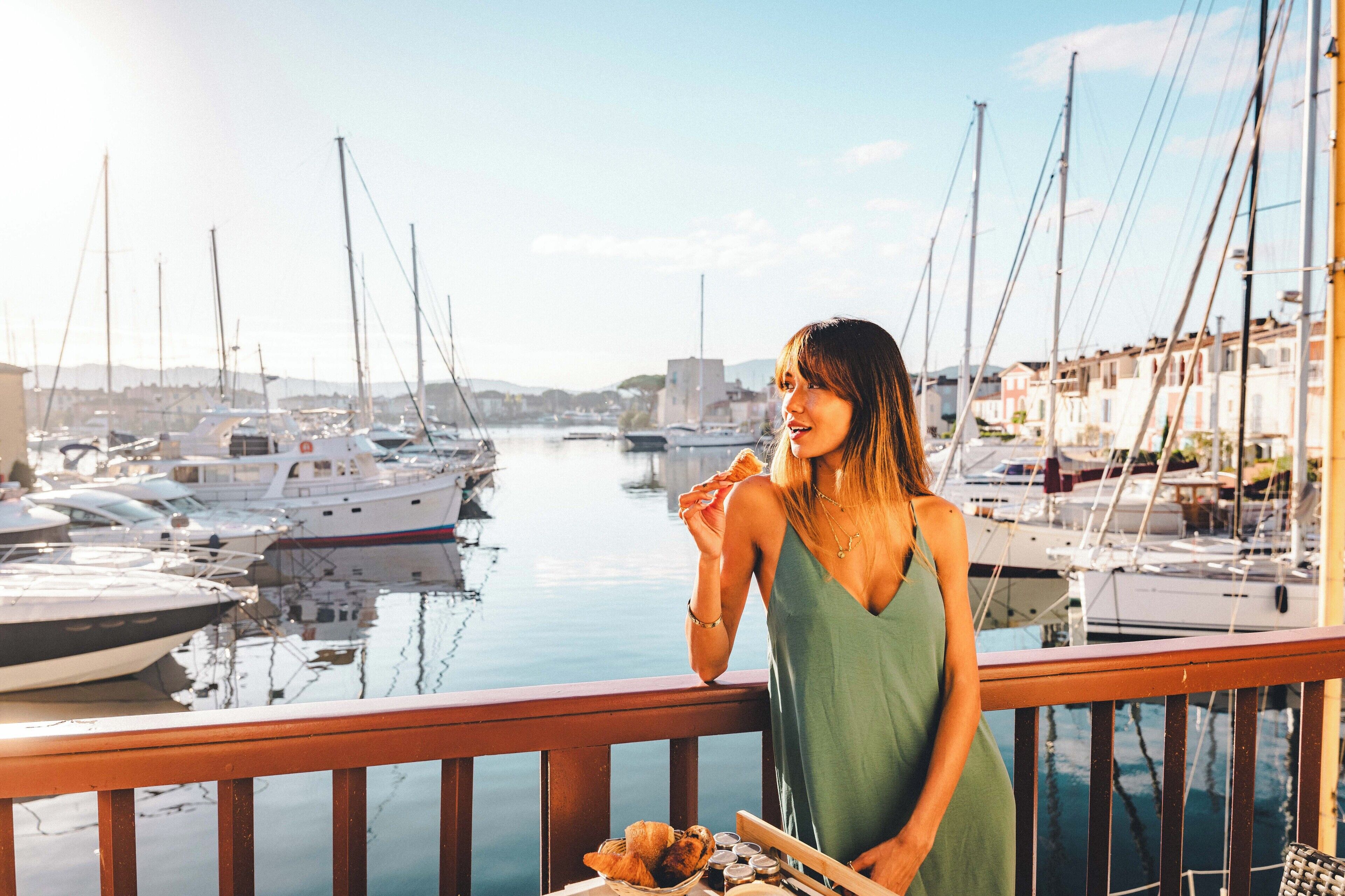 Une femme se tient sur un balcon donnant sur une marina où sont amarrés des bateaux.