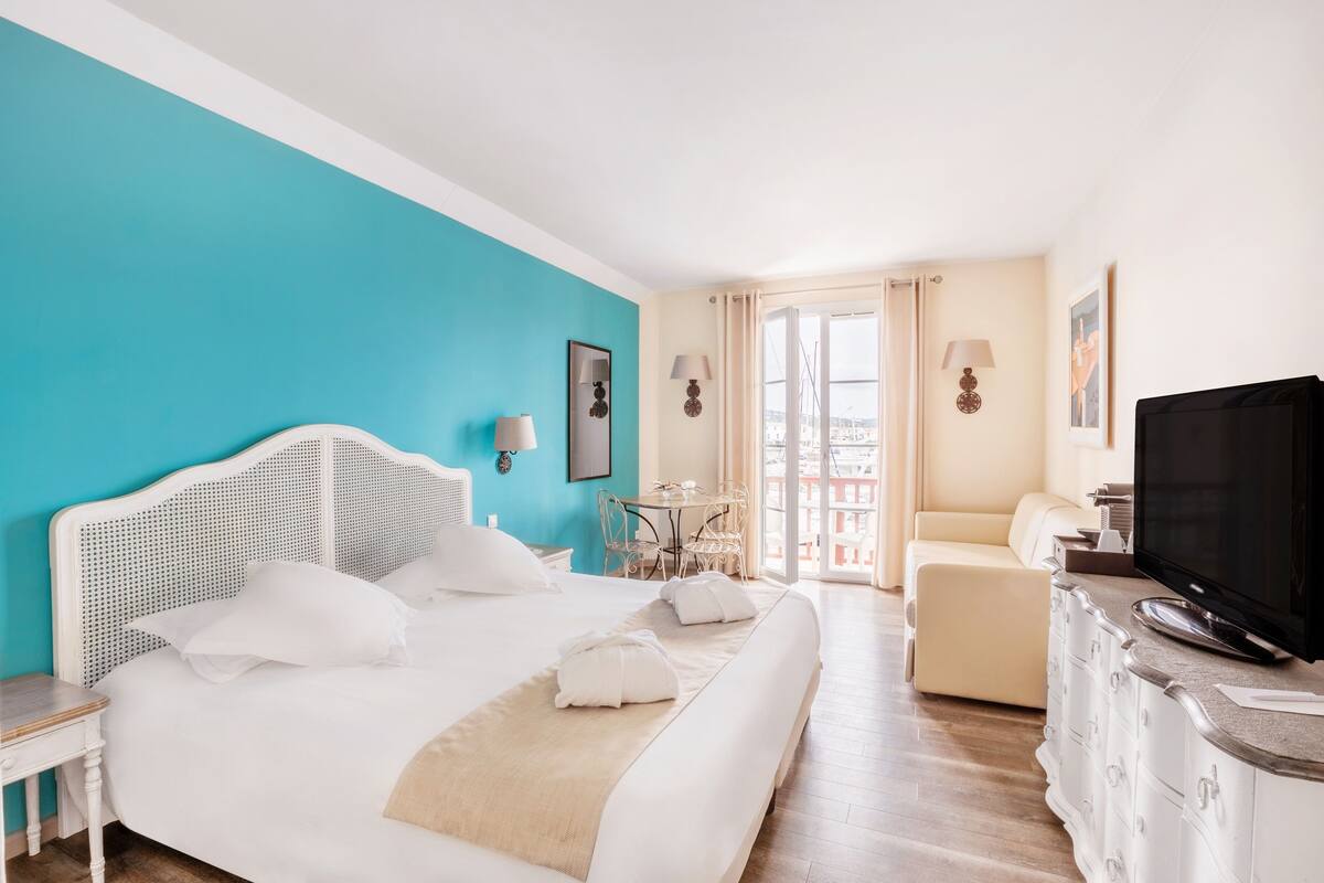 A hotel room with a bed, a TV, a desk, and a view of the outside.