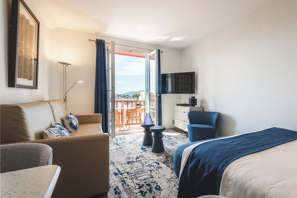 A hotel room with a bed, a sofa, a chair, a desk, a TV, and a balcony with a view.
