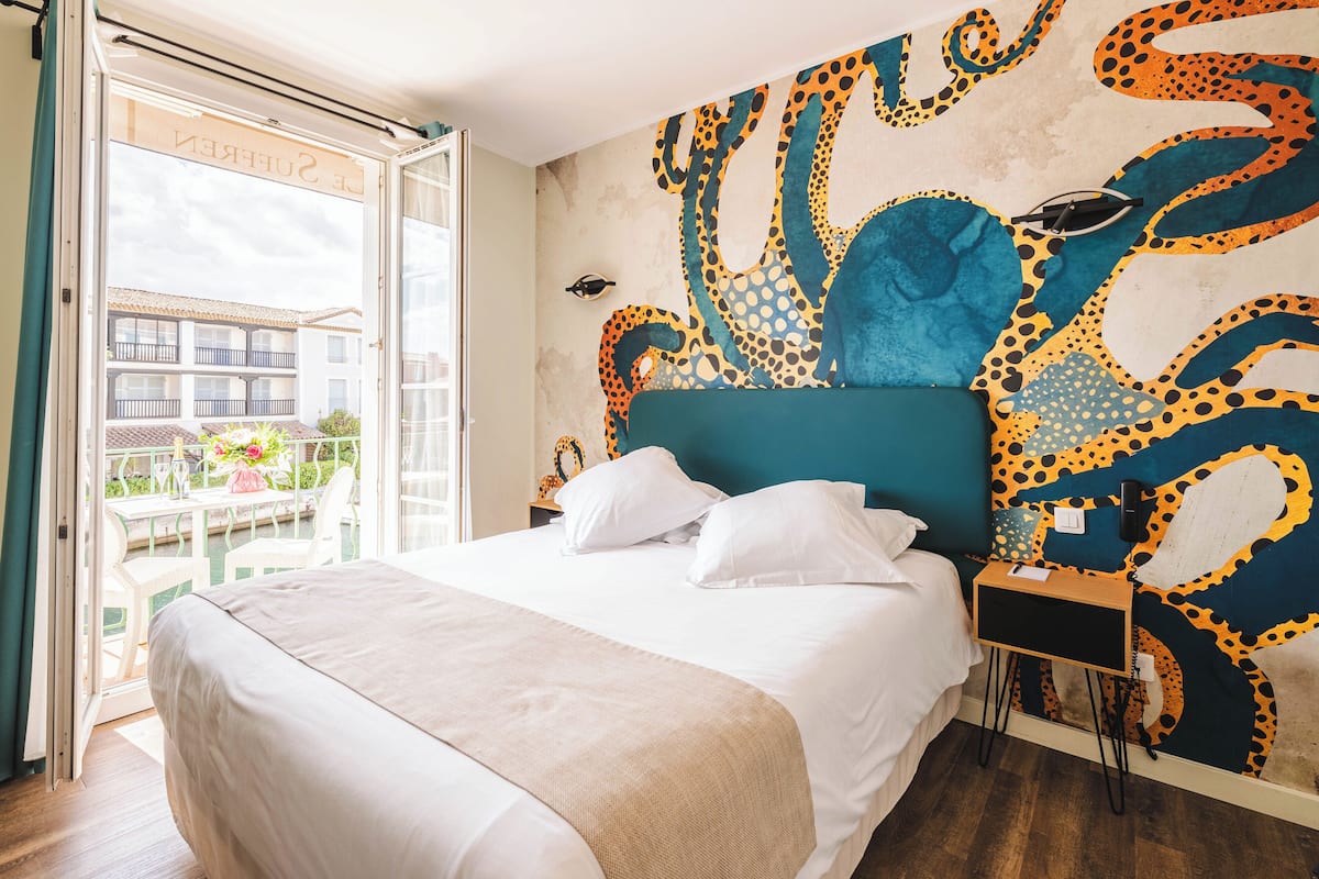 A hotel room with a large bed, a view of the outside balcony, and a colorful octopus mural on the wall.