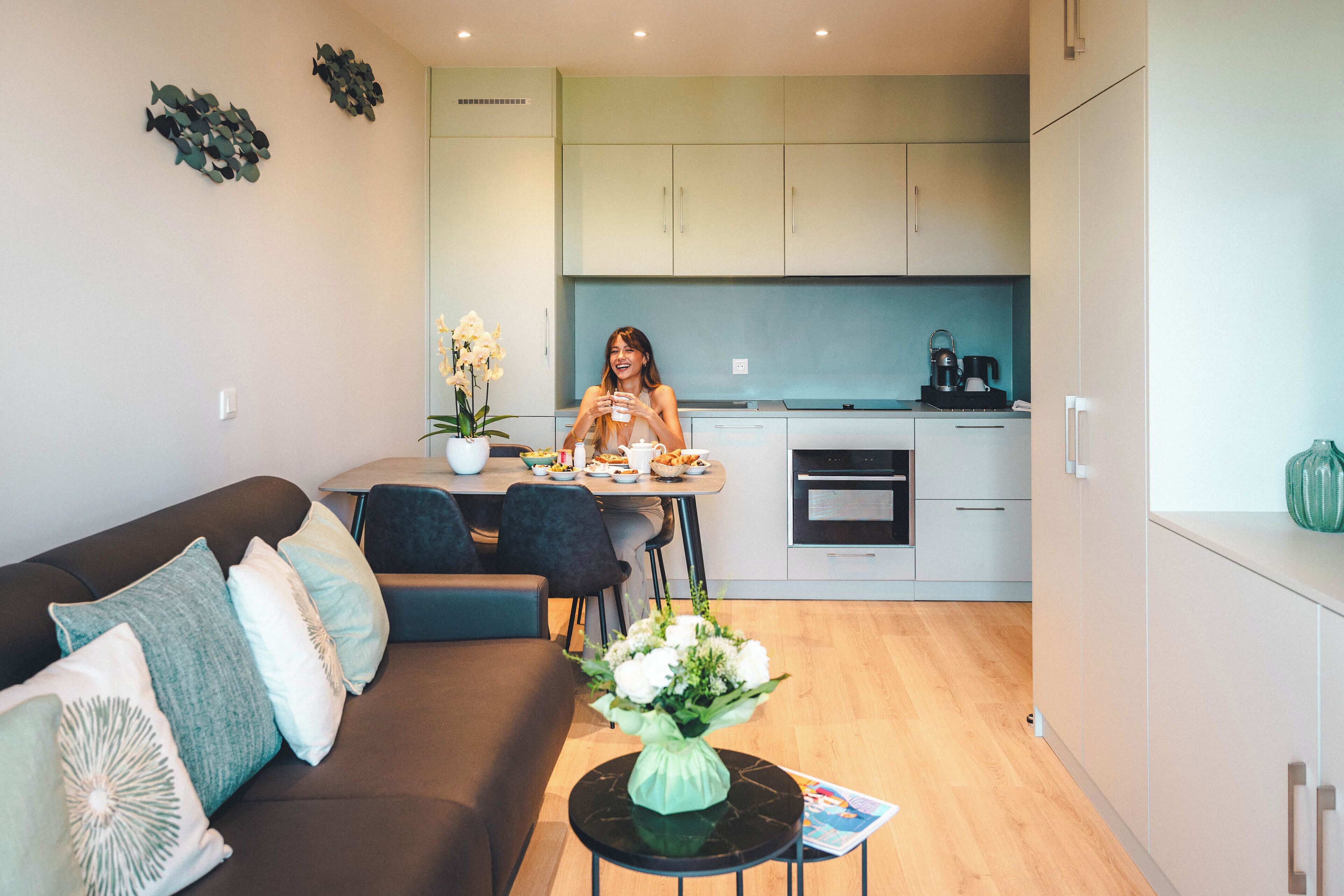 A modern living room with a sofa, a dining table, and a kitchen in the background.