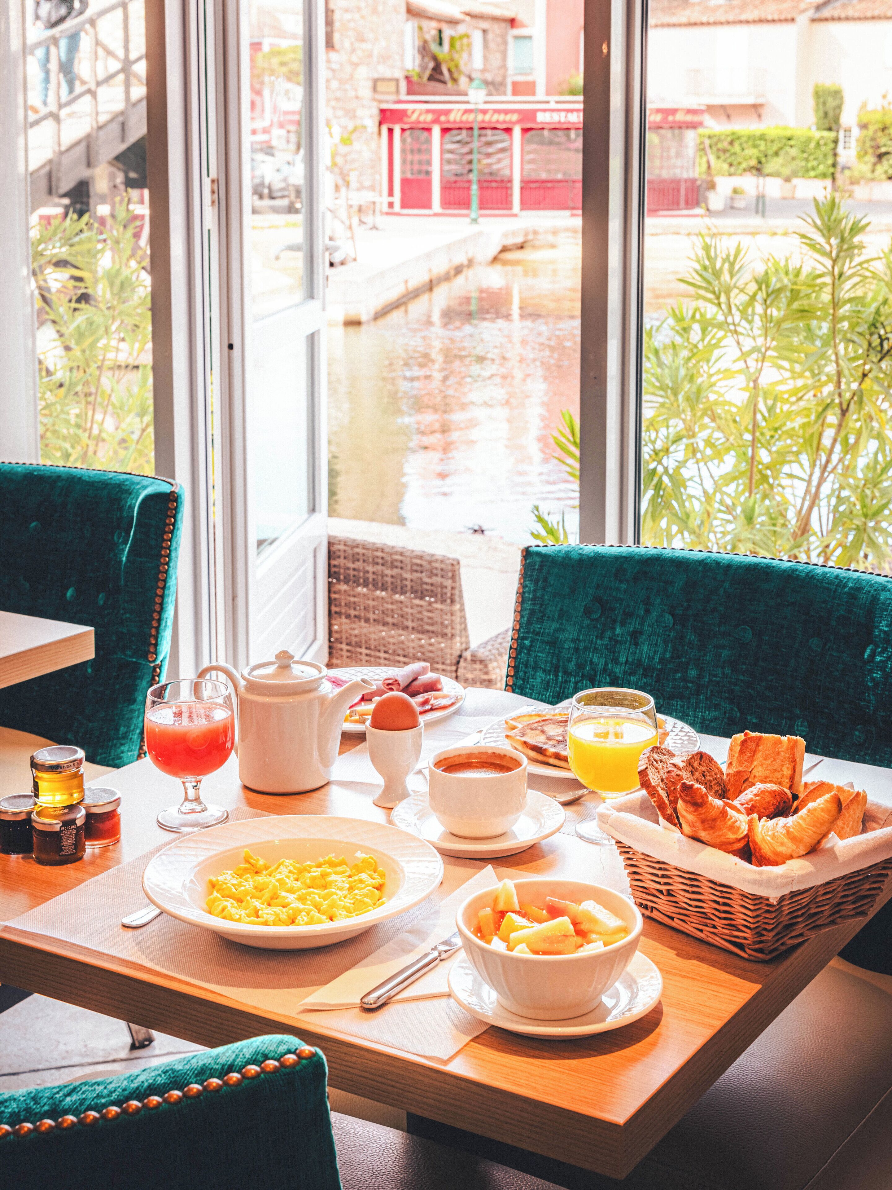 A breakfast table with various dishes, a view of a canal, and a red building in the background.