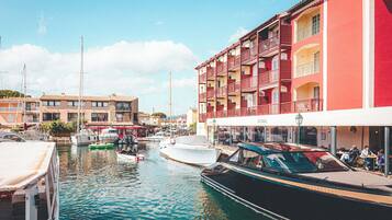 Un port de plaisance avec des bateaux amarrés, un immeuble doté de balcons et un café où des gens sont assis à l’extérieur.