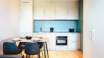 Una cocina moderna con armarios blancos, un salpicadero azul y una zona de comedor con mesa de madera y sillas oscuras.