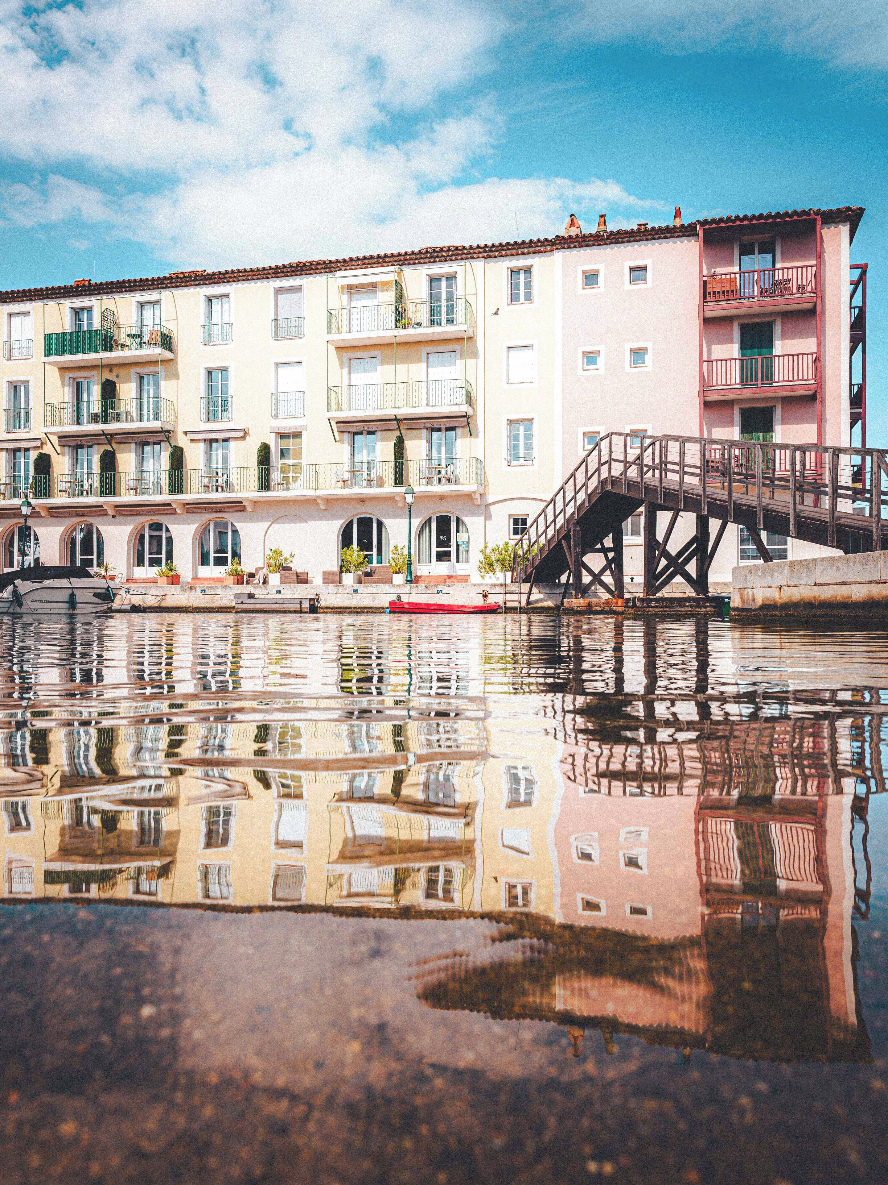 A multi-story building with balconies and a bridge over a reflective water surface.