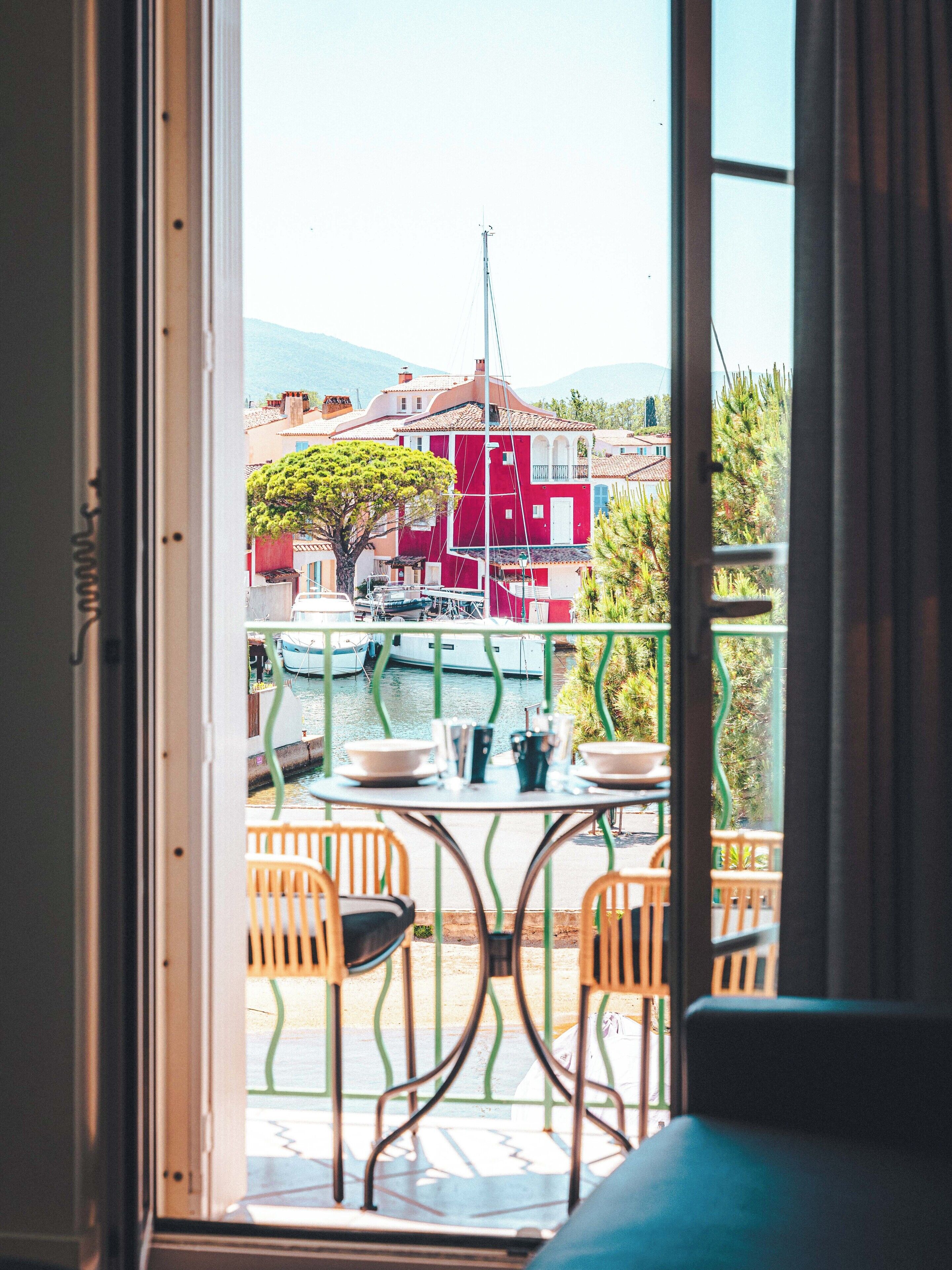 Une vue depuis un balcon, avec une table et des chaises, donnant sur une étendue d’eau et sur des bâtiments aux façades rouges et blanches.