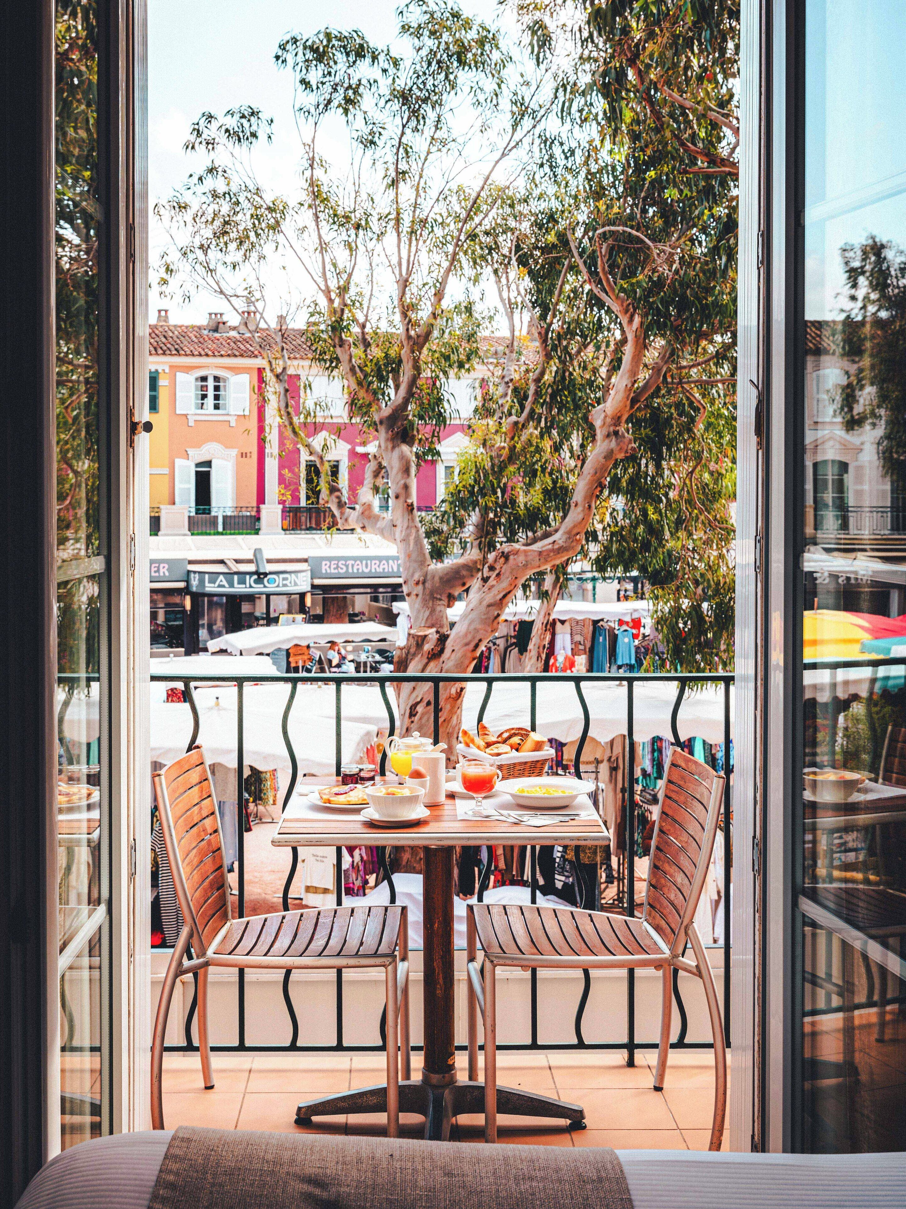 A balcony with a table set for breakfast, chairs, and a view of the cityscape.