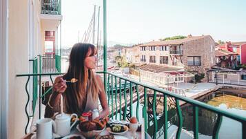 A balcony with a table set for breakfast, overlooking a canal with buildings and a bridge.