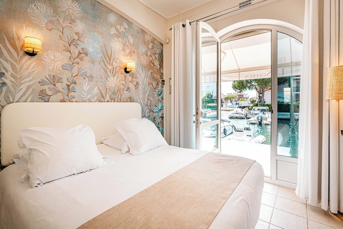A hotel room with a large bed, floral wallpaper, and a view of boats on a water body.