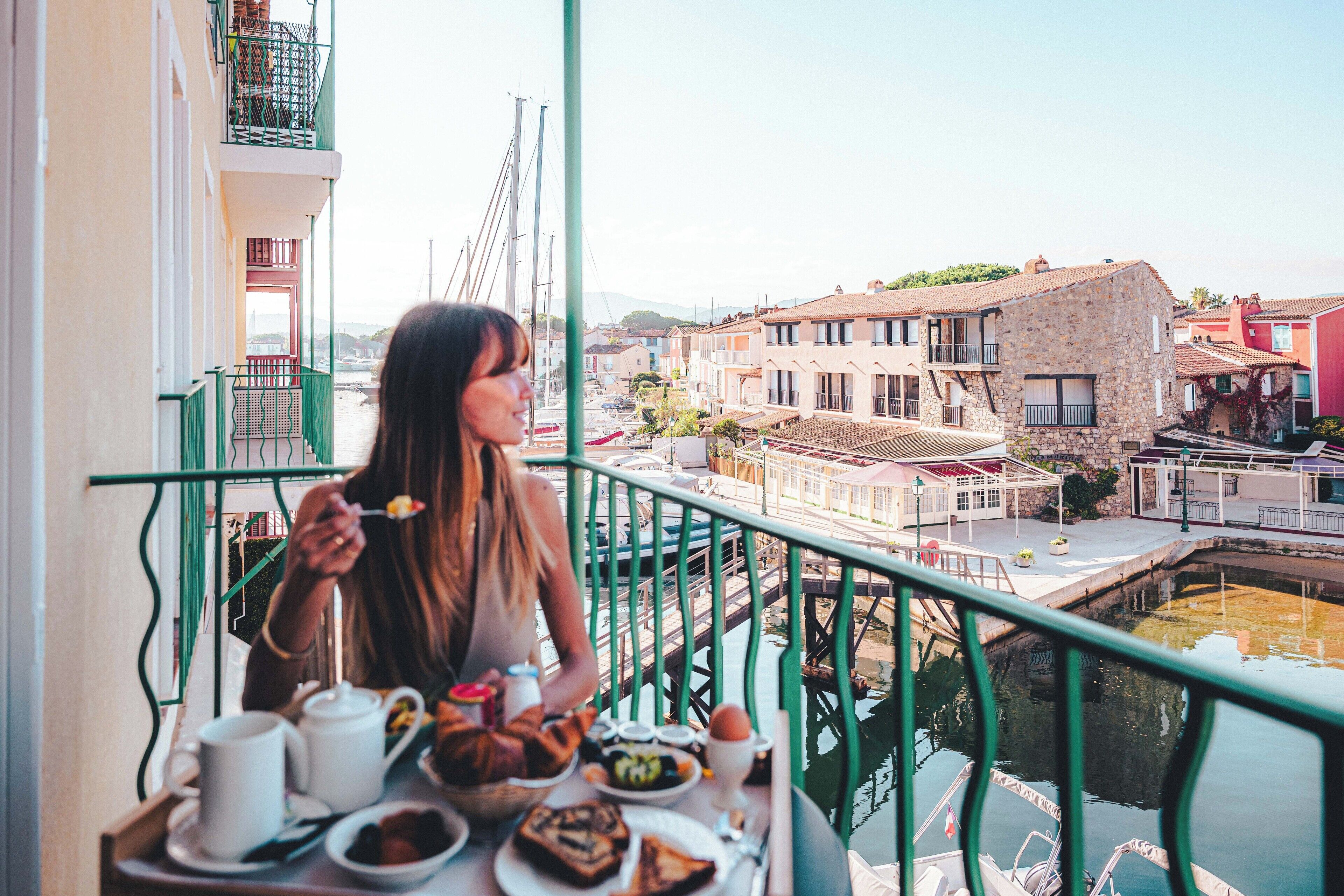 A balcony with a table set for breakfast, overlooking a canal with buildings and a bridge.