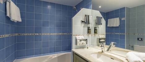 Baño con azulejos azules, una bañera, un lavabo y un espejo.