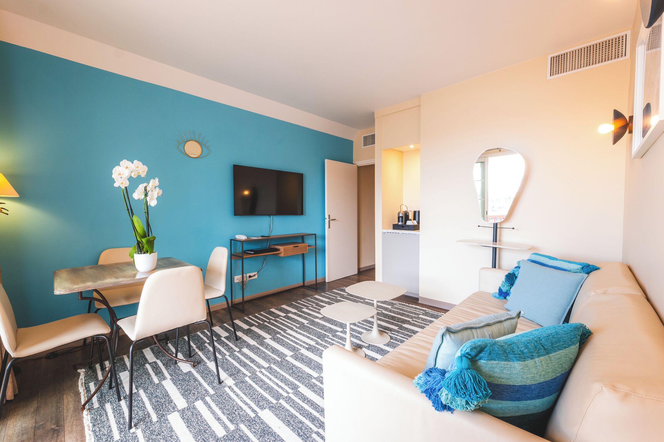 Una sala de estar moderna con una pared azul de acento, un televisor de pantalla plana, una zona de comedor con mesa y sillas, y un sofá con cojines azules.