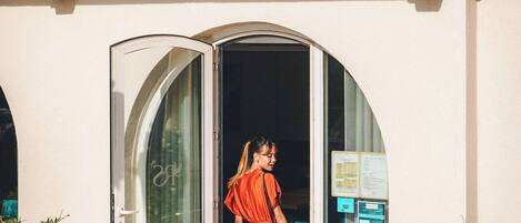A woman in a red dress exiting a building with a glass door and steps.