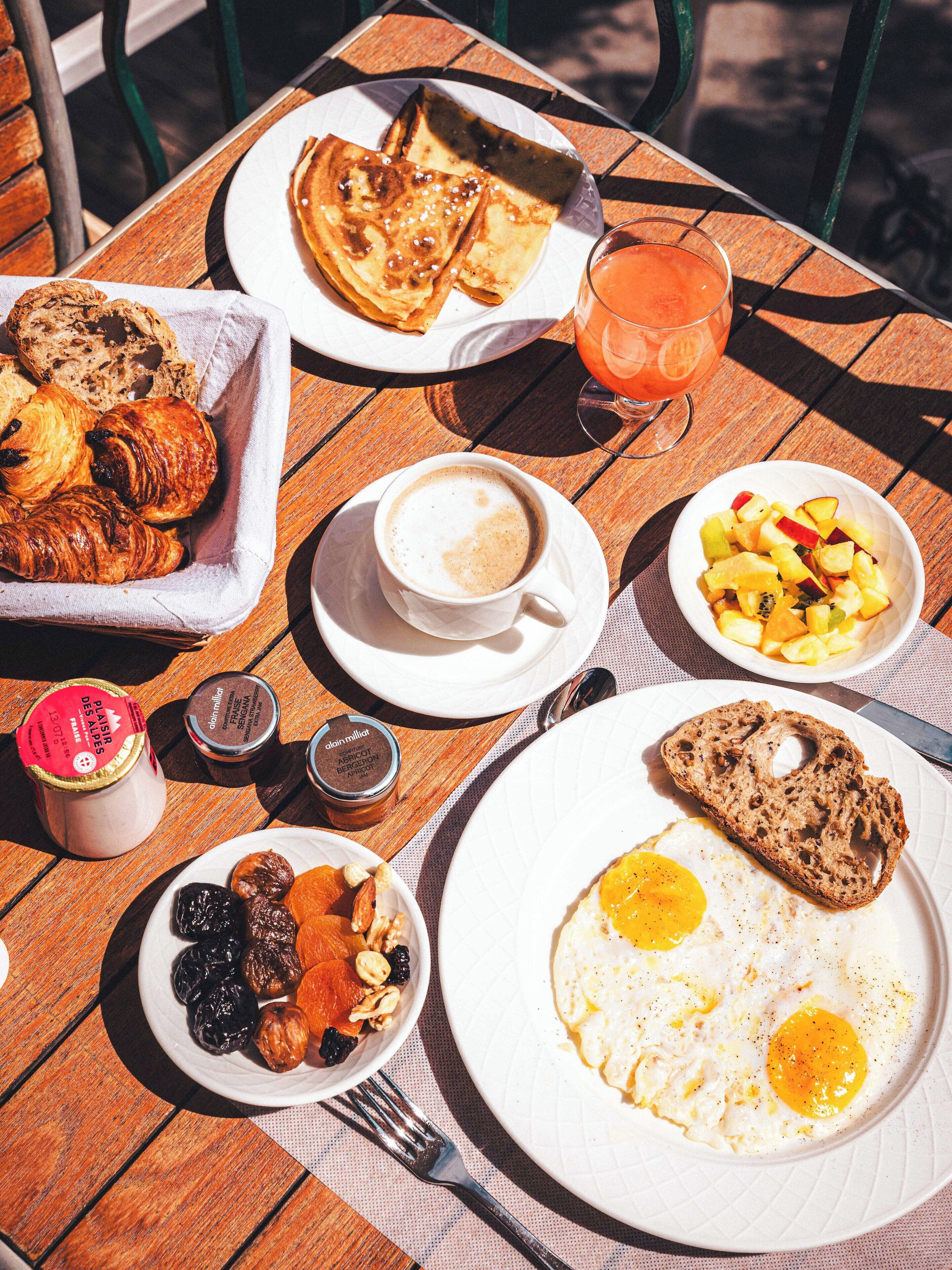 Una mesa de desayuno con cruasanes, fruta, huevos y una bebida.