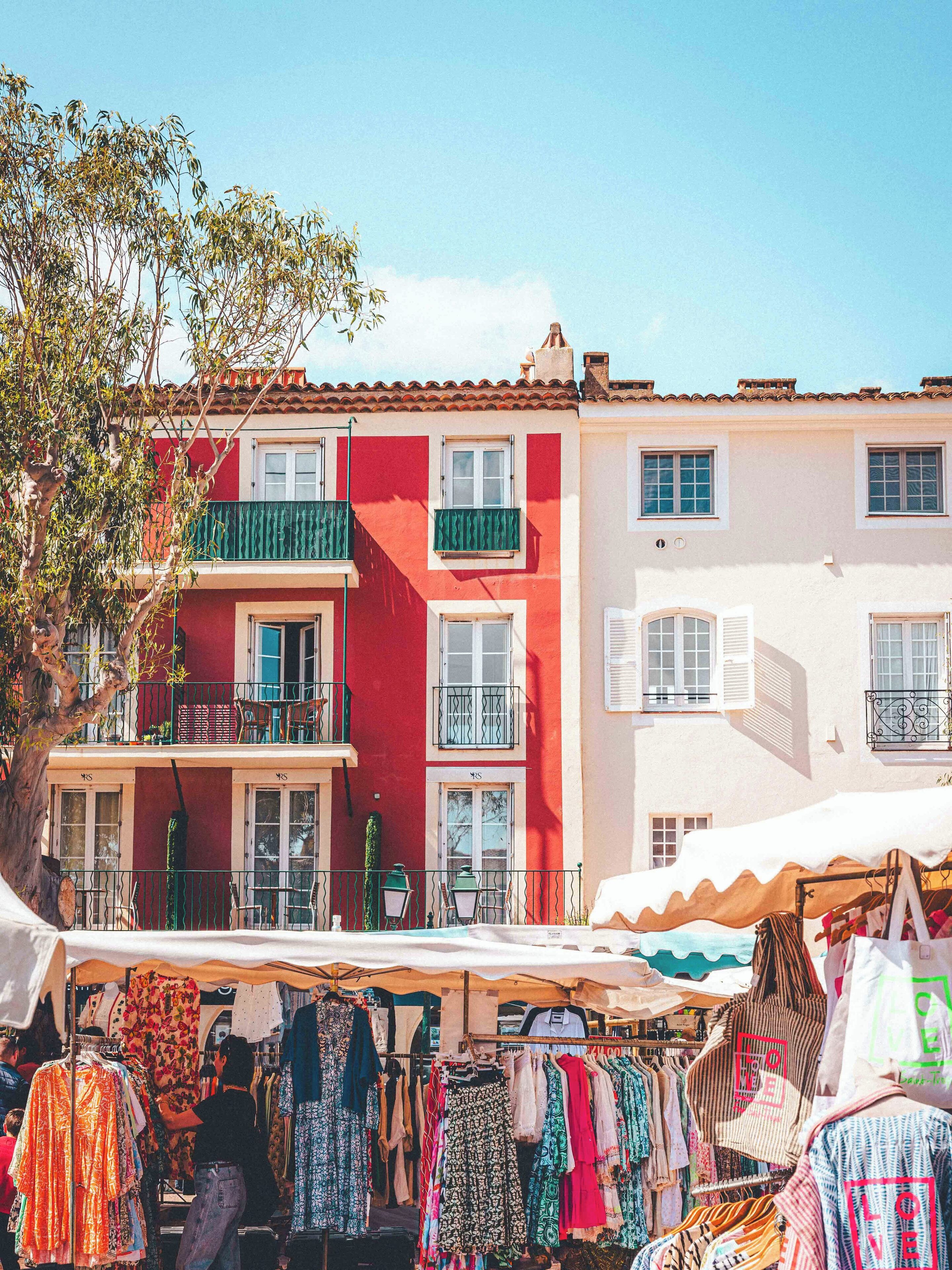 A street market with colorful clothing stalls and traditional buildings with balconies.