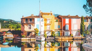A waterfront building with a reflection in the water, featuring balconies and a clear sky. -  Le Suffren Hotel, Golfe de Saint-Tropez (Grimaud)