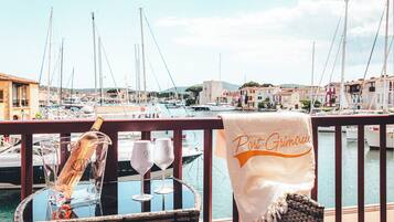 Un balcon avec une chaise en osier, une bouteille et deux verres à vin. Une serviette sur laquelle on peut lire « Port Grimaldi » est posée sur la balustrade.