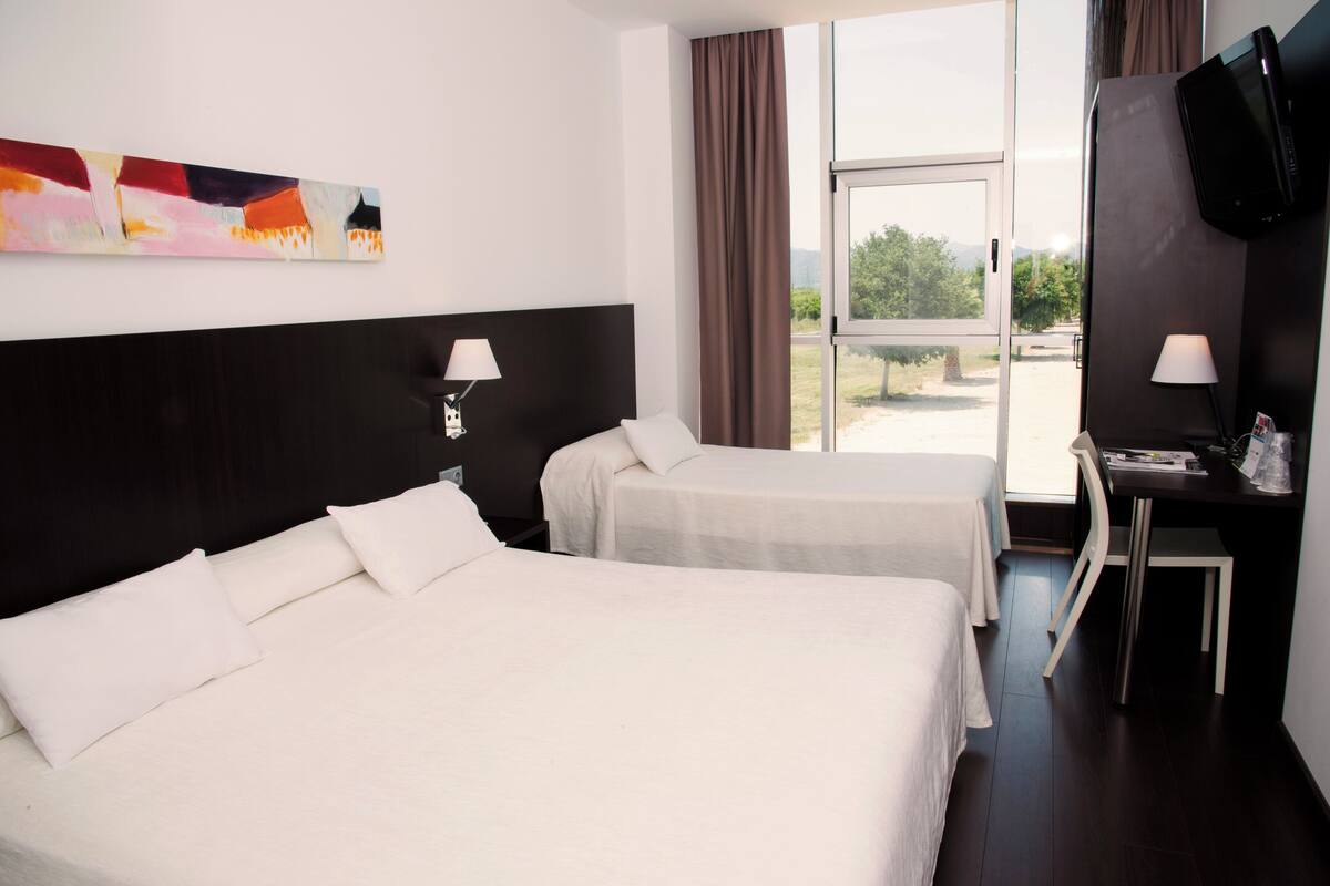 Een hotelkamer met twee bedden, een bureau met stoel, een televisie en een raam met gordijnen.