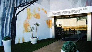 The entrance to a hotel named 'Sercotel Plaza Parc' with a modern design, featuring a large mural, potted plants, and a well-maintained pathway.