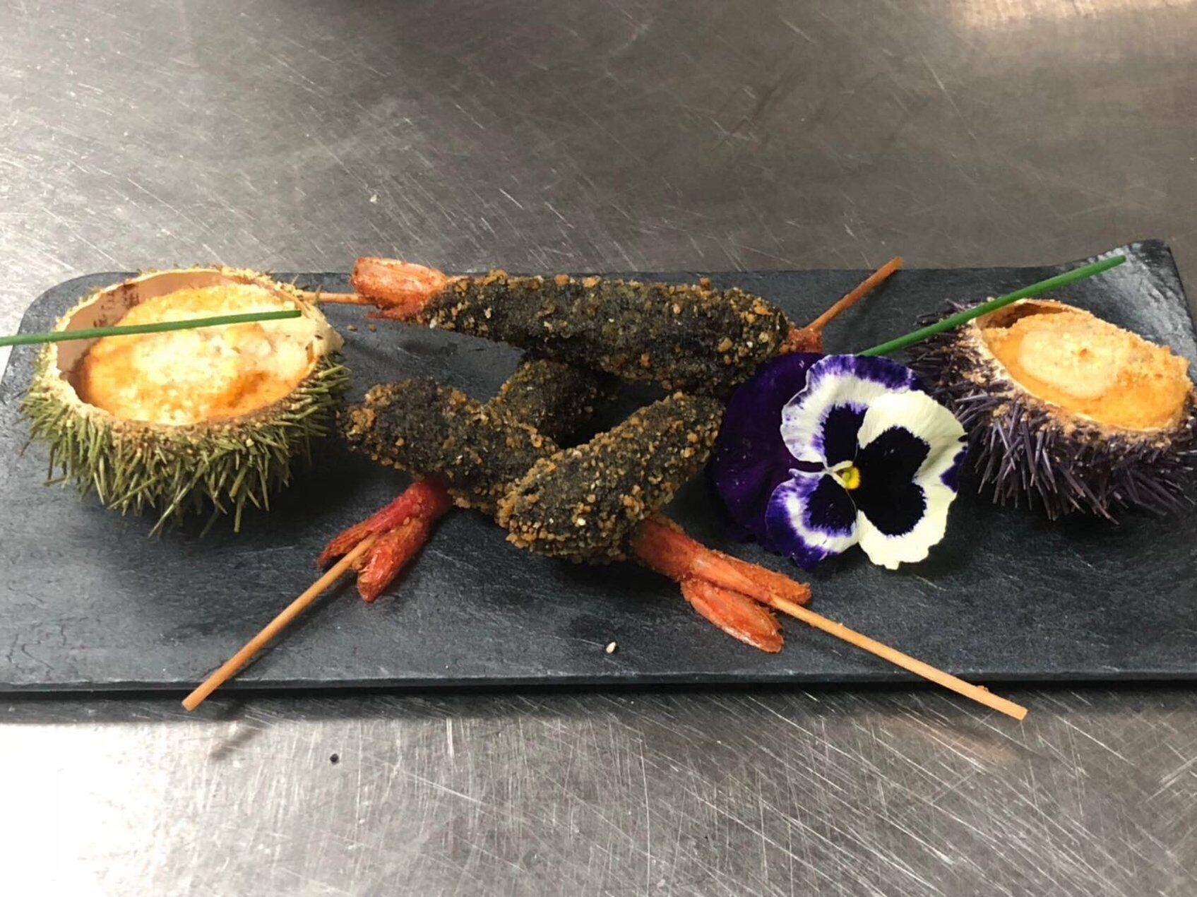A black slate serving board with various skewered items, including a sea urchin, a flower, and some vegetables.