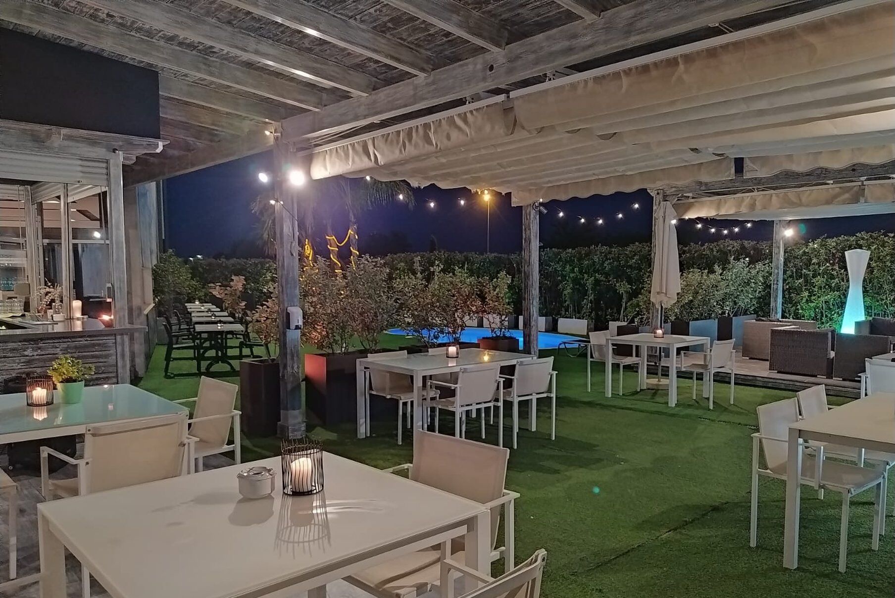 An outdoor patio area with tables and chairs, a pool, and string lights.