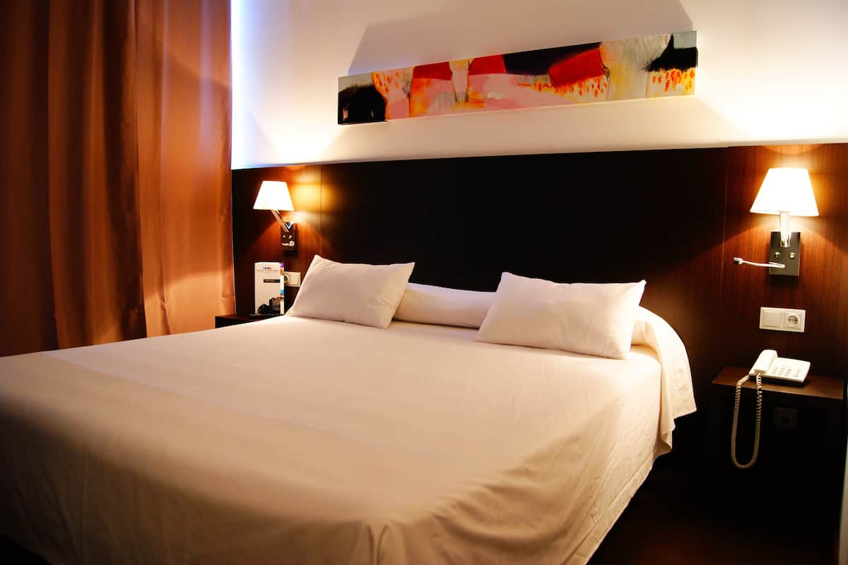 Une chambre d’hôtel avec un grand lit, deux lampes de chevet, une table de chevet avec un téléphone et un tableau au-dessus du lit.