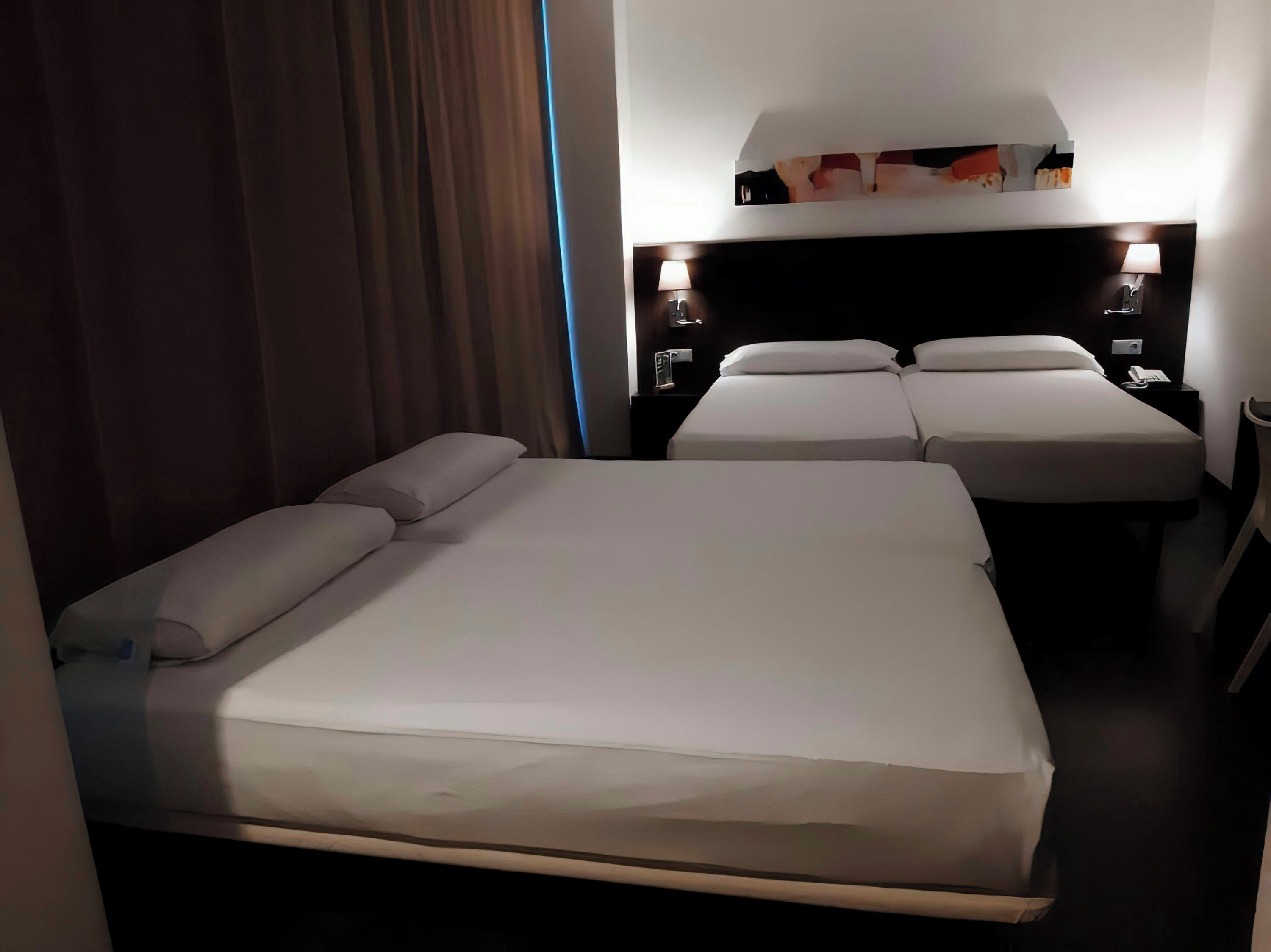 A hotel room with a large bed, two bedside tables, a nightstand, and a wall-mounted lamp.
