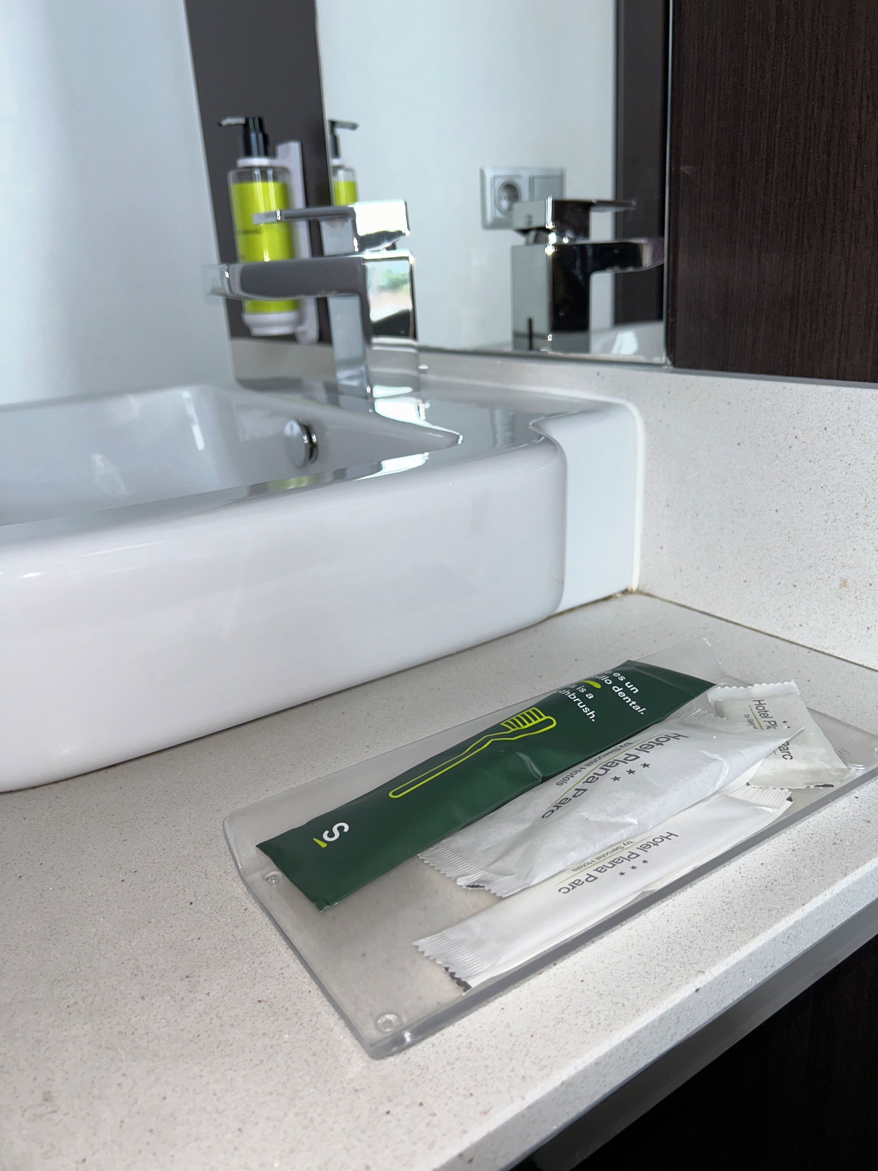 Un lavamanos con un espejo encima. Hay un paquete de artículos de tocador de hotel sobre la encimera.