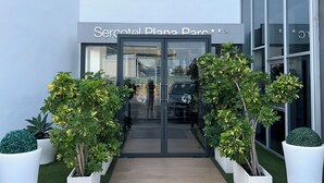 A hotel entrance with a glass door, a sign above reading "Hotel Planar Park," and a pathway flanked by potted plants.