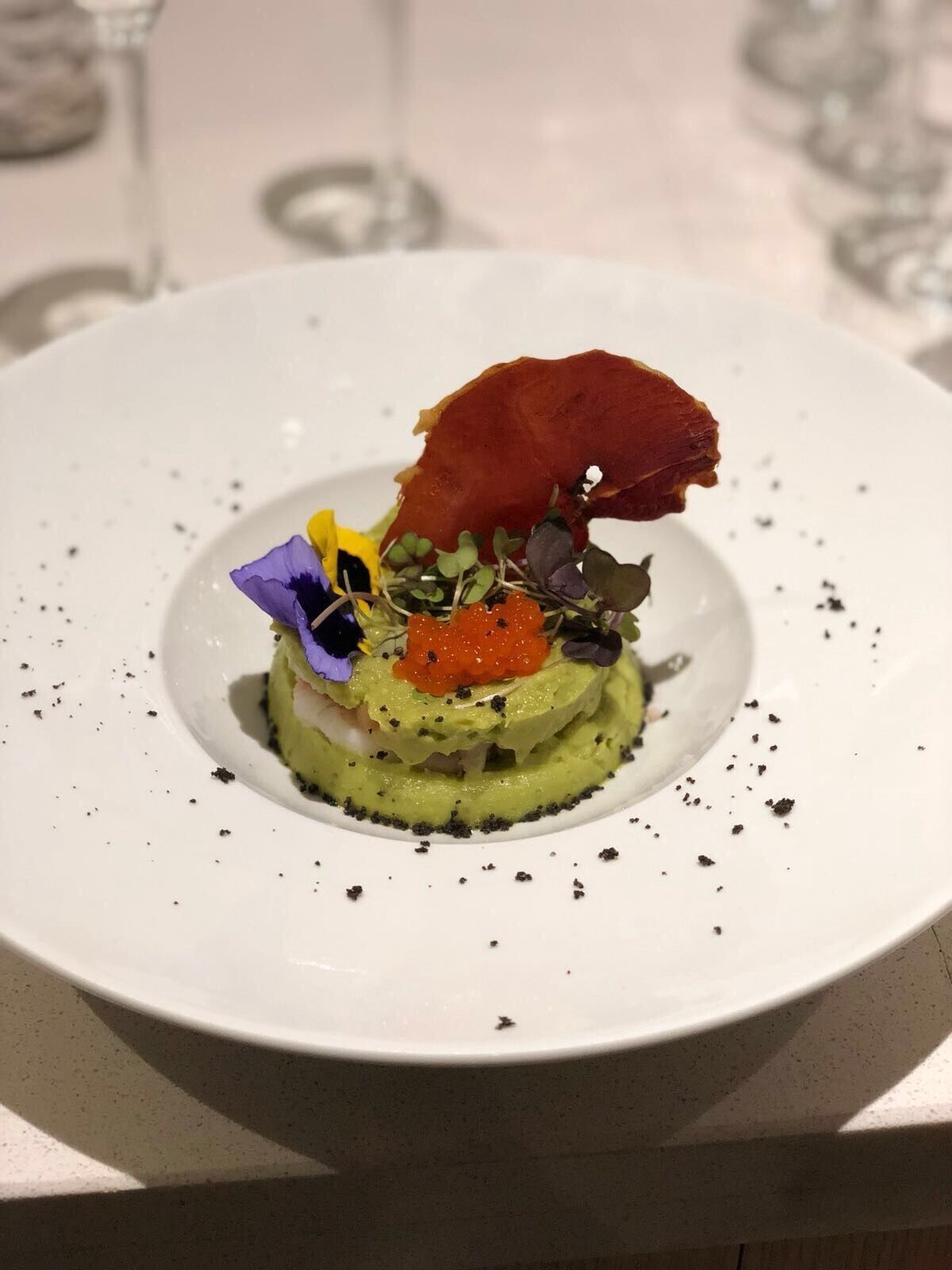 A white plate with a layered dish, garnished with a red leaf, purple flower, and orange caviar.