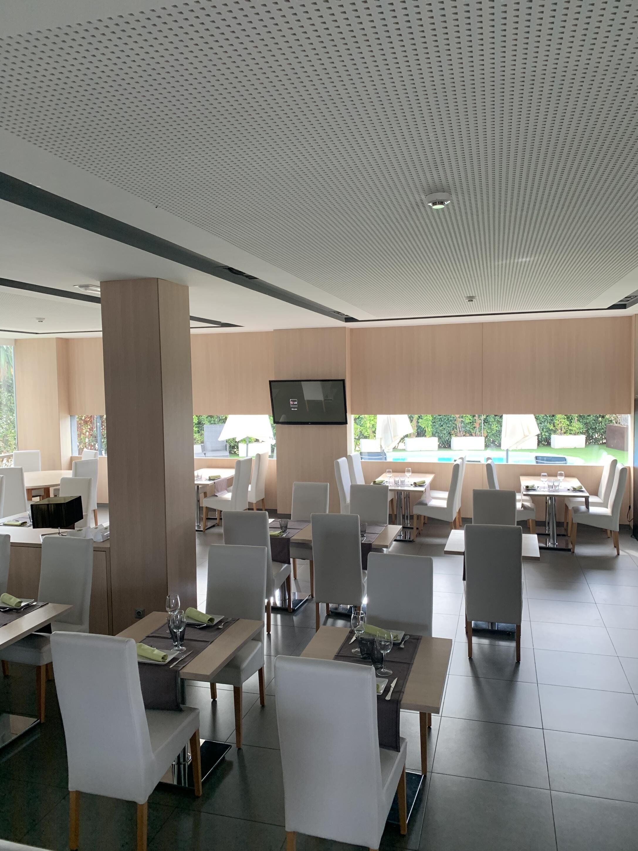 Ein modernes Restaurant mit hoher Decke, weißen Stühlen und Tischen, die zum Essen bereitstehen.