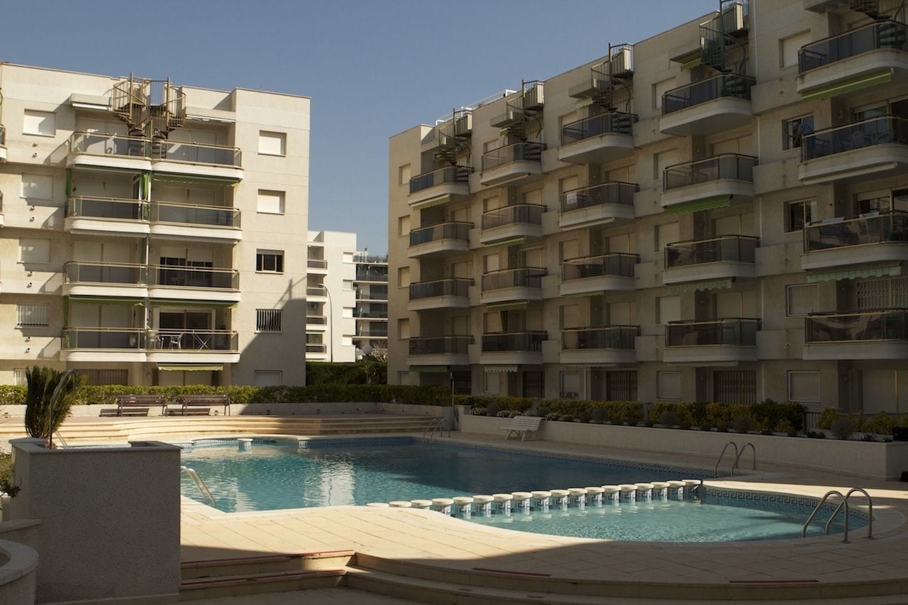 A modern apartment building with a swimming pool, balconies, and a clear sky.