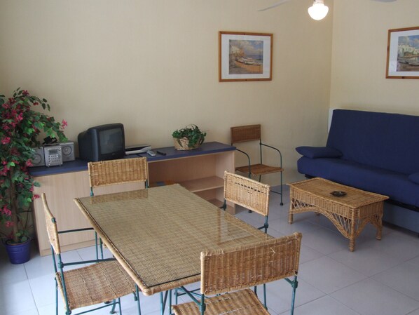 A room with a dining table, chairs, a sofa, a television, and two framed pictures on the wall. - Apartamentos Somni Cambrils (Cambrils)