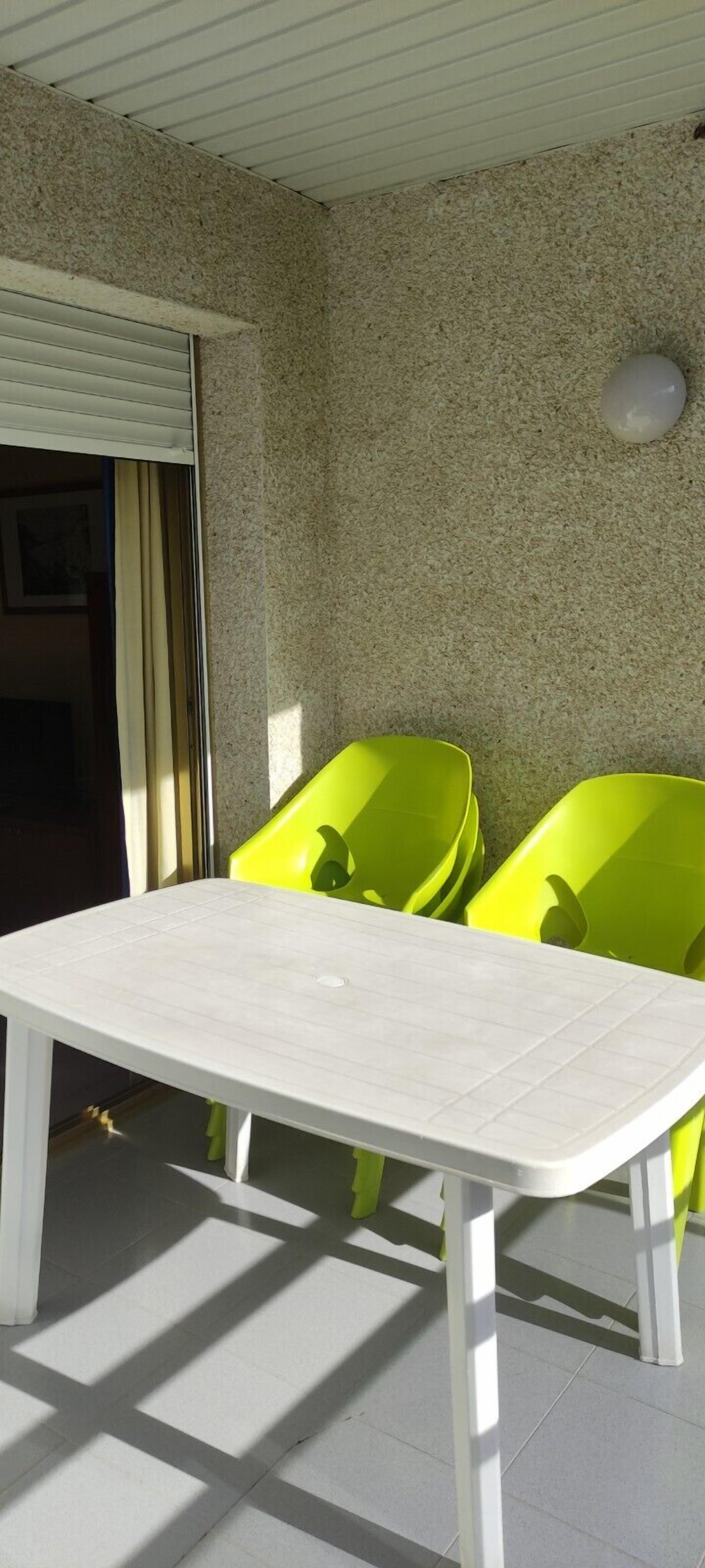 Une pièce avec une table blanche, deux chaises vertes, un plafond blanc et un mur à texture.