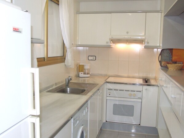 Una cocina compacta con lavabo, cafetera, lavadora y estufa.