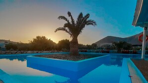 A pool with a palm tree in the center, surrounded by a stone border. - Perissa Hotel (Santorini)