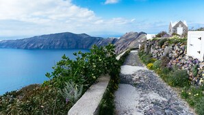 A coastal path with a stone wall and a white building with a pointed roof. - Perissa Hotel (Santorini)