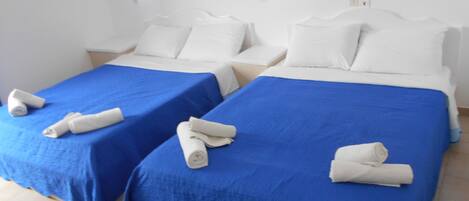 Two twin beds with blue bedspreads and white pillows, each with a rolled towel.
