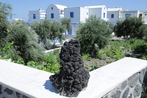 Formación rocosa volcánica en un jardín con edificios blancos al fondo.