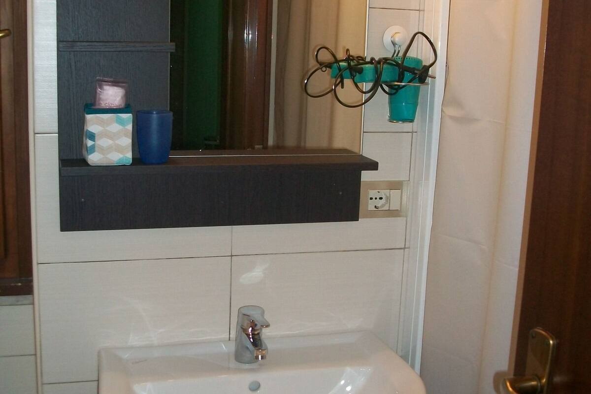 A bathroom with a white sink, a mirror above it, and a shelf with toiletries.