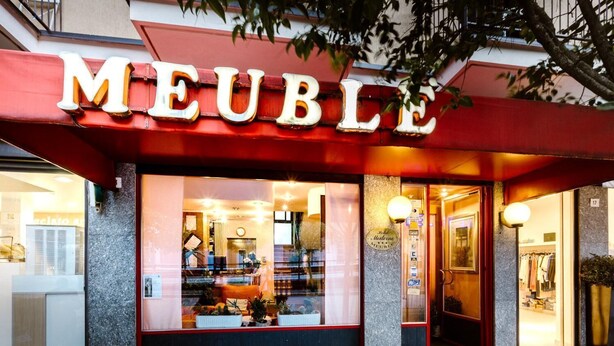 Ein Hotel Eingang mit einer roten Markise, auf der der Name 'MEUBLE' steht.