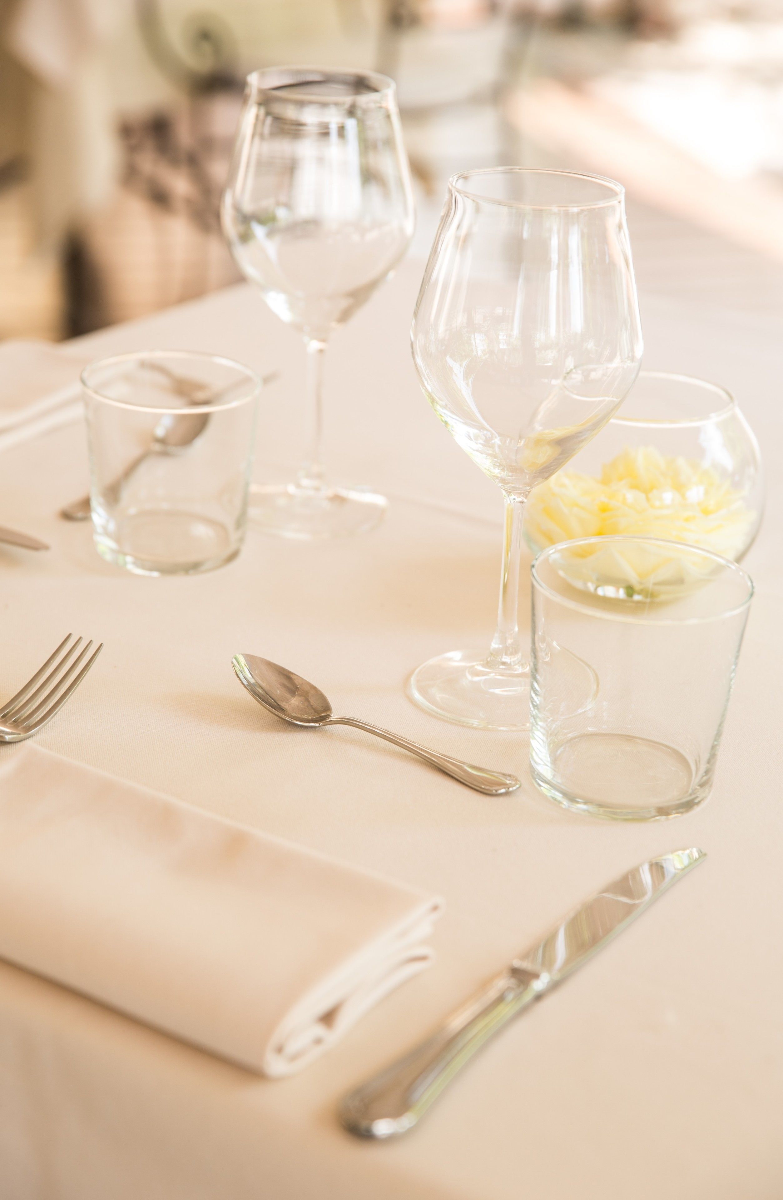 A table set with clear glassware, a folded napkin, and a bowl of yellow flowers.