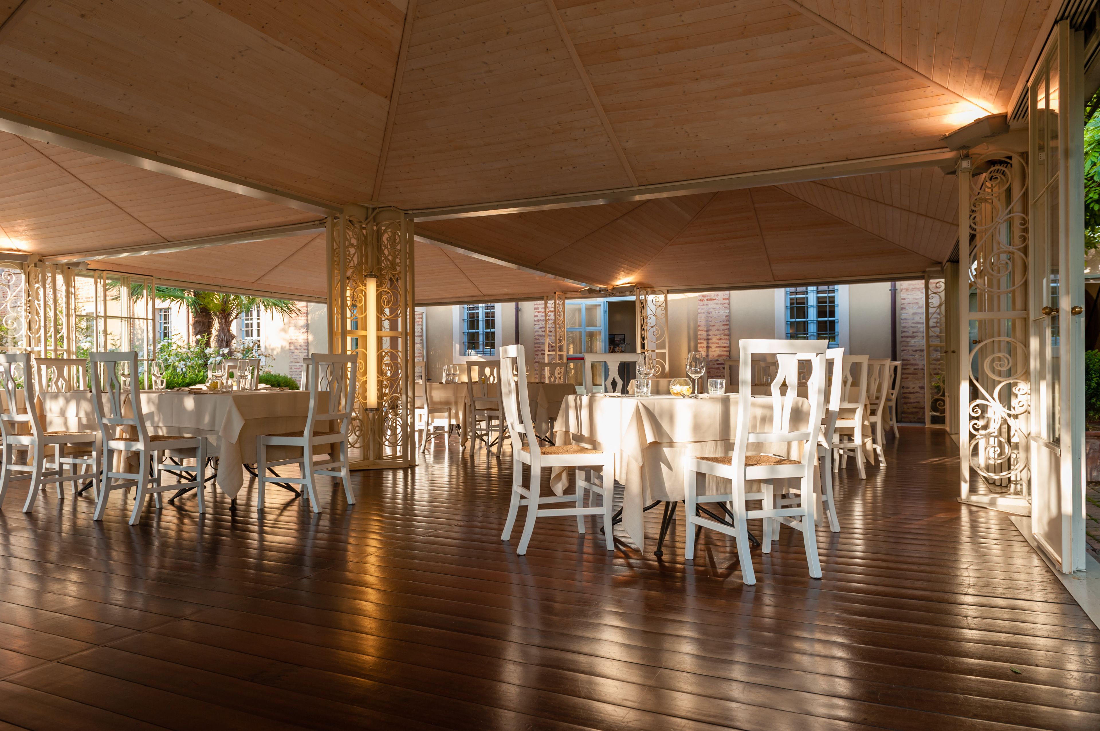 Un comedor interior con varias mesas y sillas, suelo de madera y una gran estructura similar a una carpa en el techo.